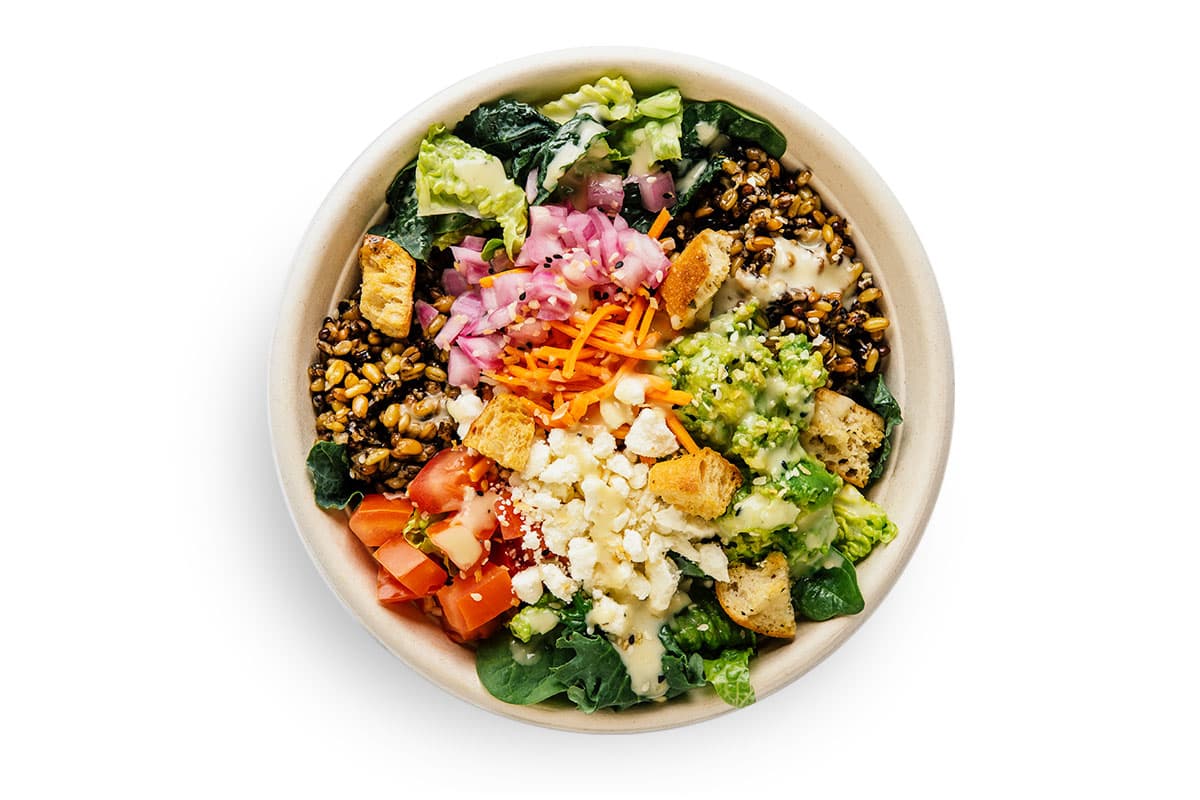 Aerial view of a bowl with rice, veggies, avocado, feta cheese, pickled carrots, pickled onion, tomatoes, croutons.