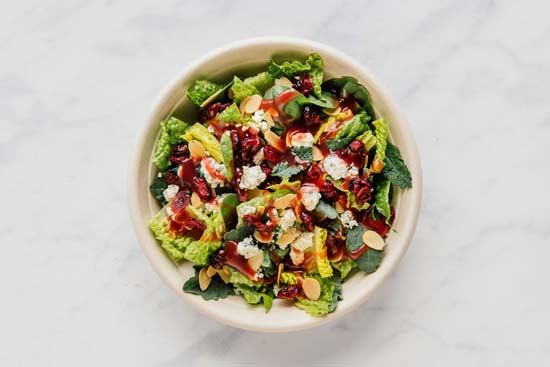 Aerial view of a salad bowl that has green veggies, cranberries, gorgonzola, almonds, and vinaigrette