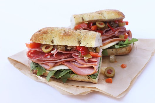 A sandwich cut in half that has ham, salami, provolone, giardiniera, and kale on focaccia bread.