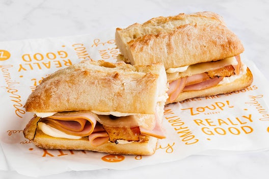 A sandwich cut in half that has ham, bacon, swiss cheese, and an aioli on ciabatta bread.