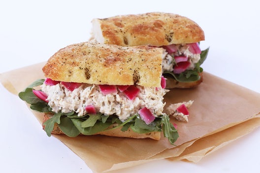 A sandwich cut in half that has tuna, pickled onions, and kale on focaccia bread.