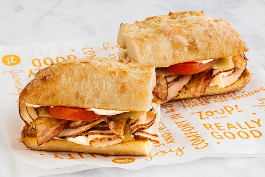 A sandwich cut in half that has turkey, bacon, swiss cheese, tomatoes, and mayo on ciabatta bread.