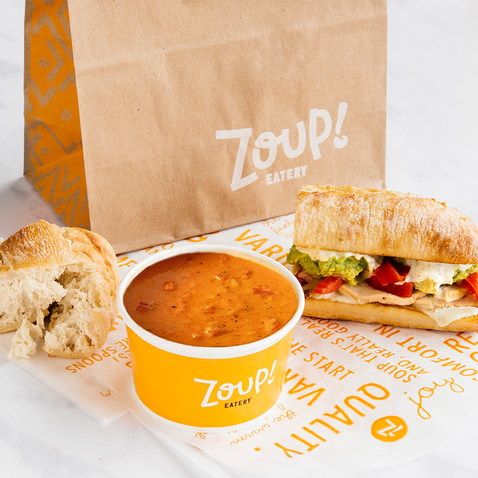 Zoup! Eatery takeout with tomato soup, a chicken sandwich with guacamole and peppers, and a piece of torn bread.