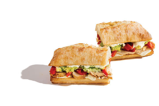 Two grilled chicken sandwiches with guacamole, diced tomatoes, and lettuce on ciabatta rolls.