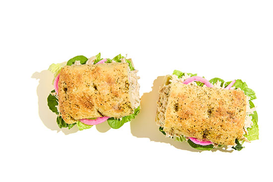 Shredded chicken sandwiches with leafy greens and pickled onions on herb focaccia bread.
