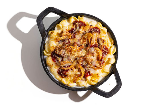 Skillet of mac and cheese topped with crispy onions, BBQ sauce, and breadcrumbs.
