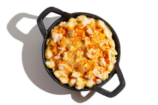 Skillet of mac and cheese with chunks of buffalo chicken and a light dusting of seasoning.