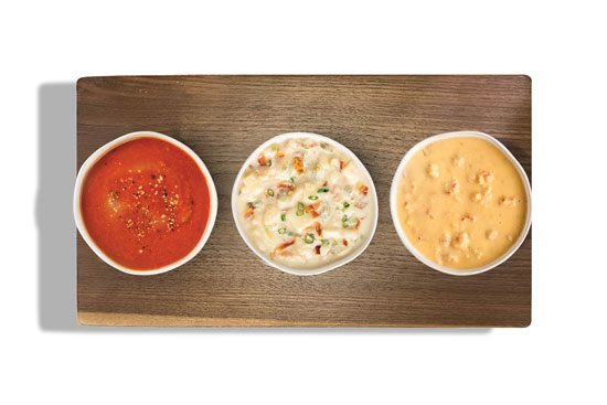 Trio of soups on a wooden board: tomato basil, loaded baked potato, and lobster bisque.