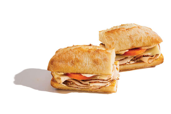 Sliced turkey sandwiches with tomato and melted cheese on ciabatta rolls.