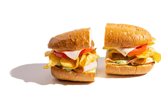 Sandwiches layered with chips, tomato, cheese, and a green sauce on toasted buns.