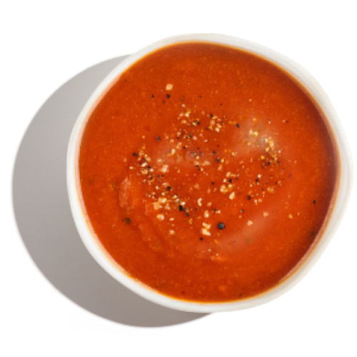 Bowl of tomato soup topped with cracked black pepper, photographed from above.