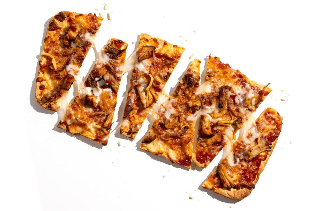 Sliced BBQ chicken flatbread pizza with melted cheese and grilled onions.