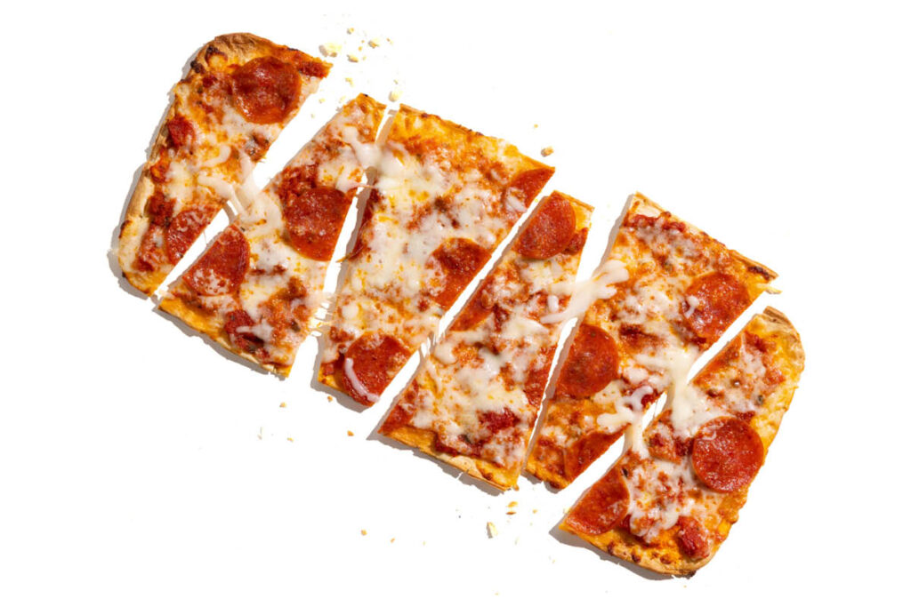 Sliced Margherita flatbread pizza with tomato sauce, fresh mozzarella, cherry tomatoes, and basil pesto.