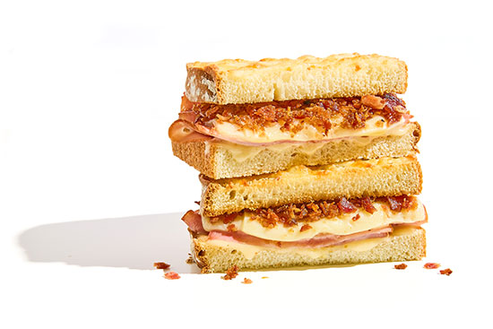 Stacked sandwich halves with ham, melted cheese, and bacon bits on toasted bread.