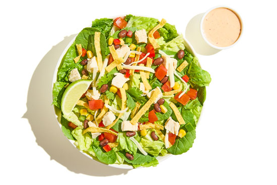 Southwest salad with chicken, black beans, corn, peppers, shredded cheese, tortilla strips, and lime wedge, served with dressing.