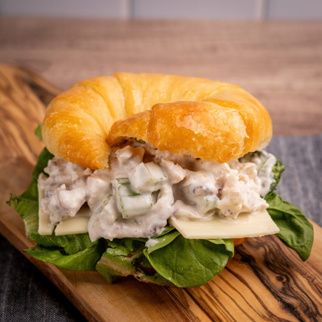 A croissant sandwich filled with creamy chicken salad, leafy greens, and cheese.
