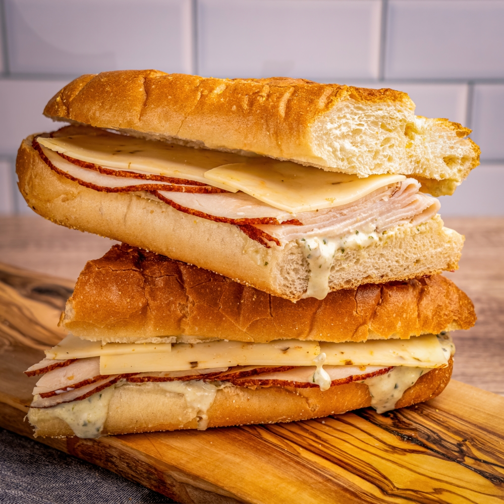 A stacked sandwich with sliced turkey, cheese, and creamy herb sauce on a toasted baguette.