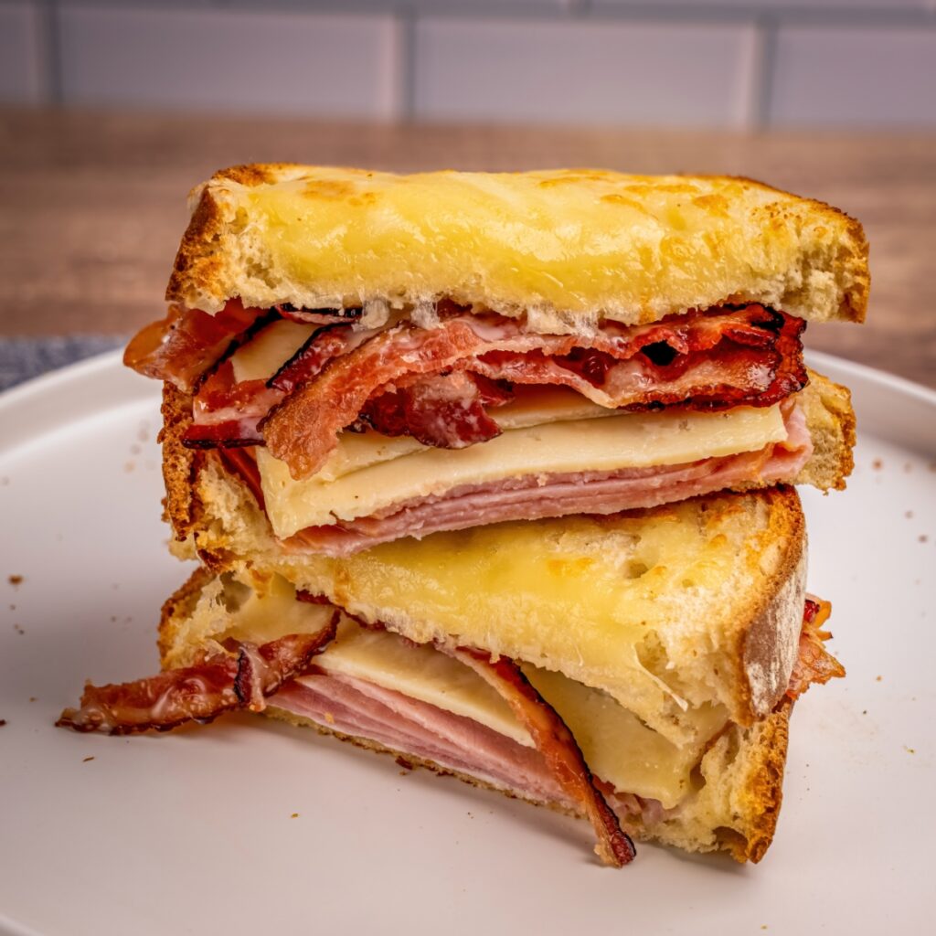 A grilled sandwich stacked with melted cheese, ham, and crispy bacon on toasted bread.