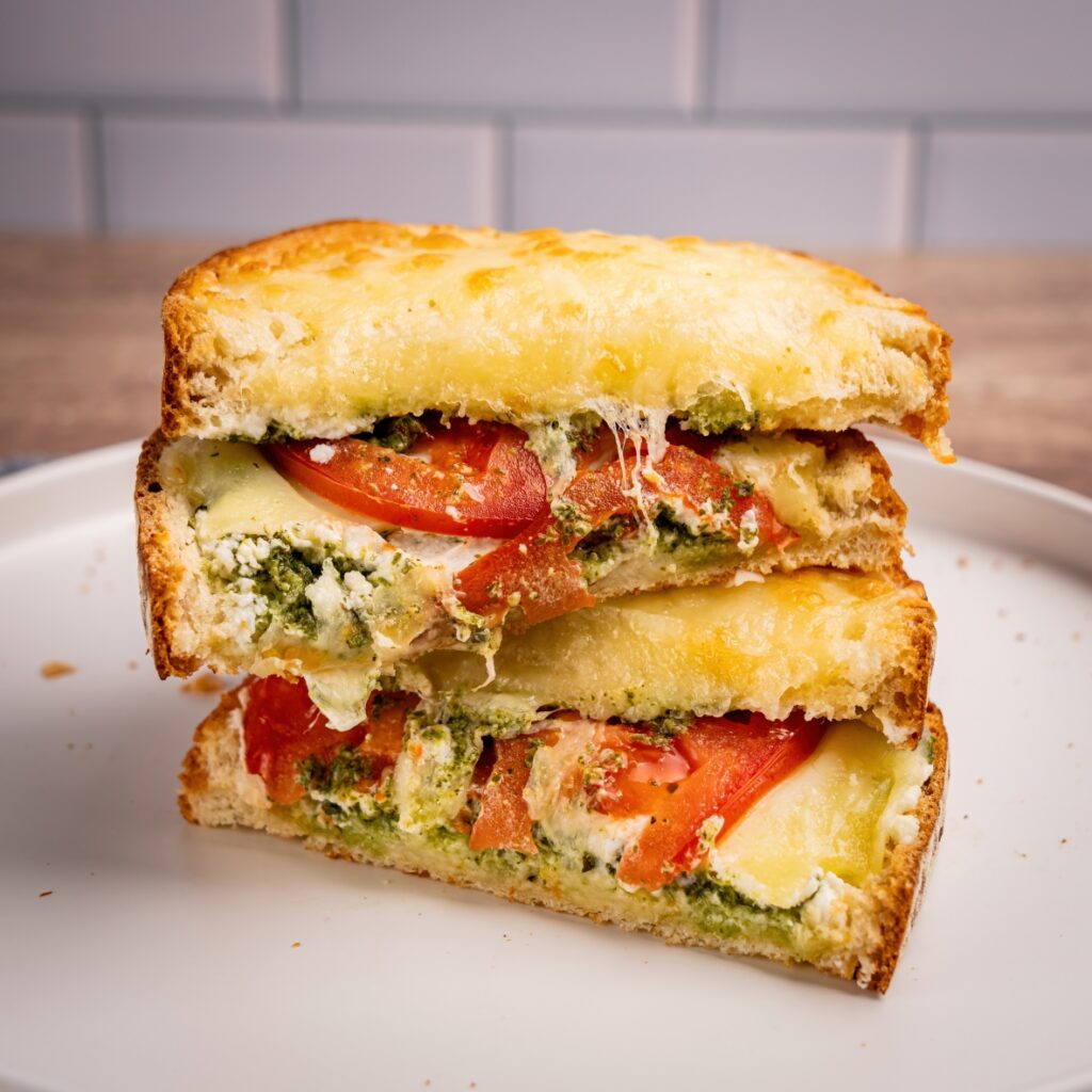 A grilled sandwich filled with melted cheese, tomatoes, and pesto on toasted bread.