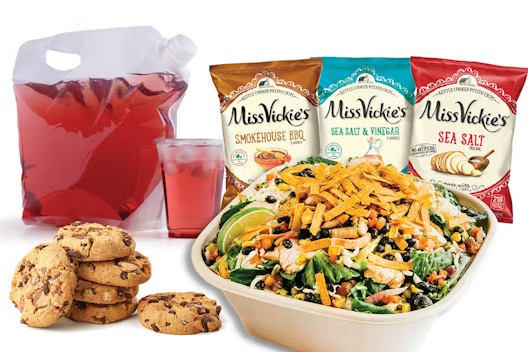 A salad with grilled chicken and tortilla strips, served with fruit punch, chocolate chip cookies, and three bags of Miss Vickie’s chips.