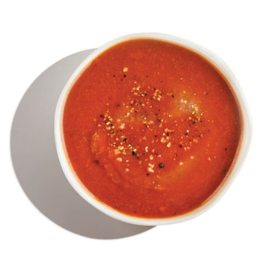 Overhead view of smooth tomato soup in a white bowl, topped with cracked black pepper and seasoning.