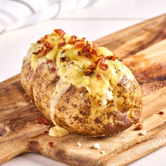 aked potato topped with creamy cheese sauce and crispy bacon crumbles on a wooden board.